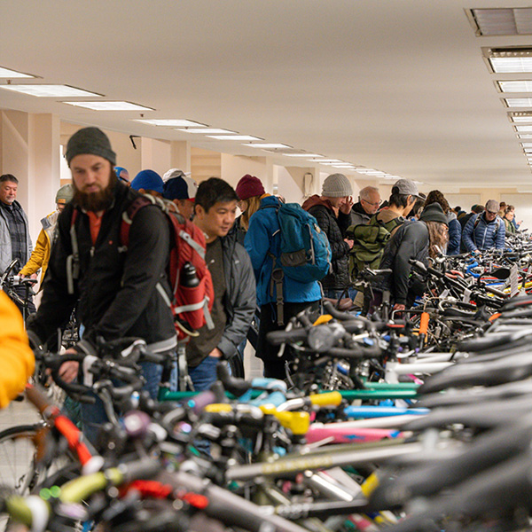 A large group of people standing in a room filled with various bicycles, engaged in conversation and activities.