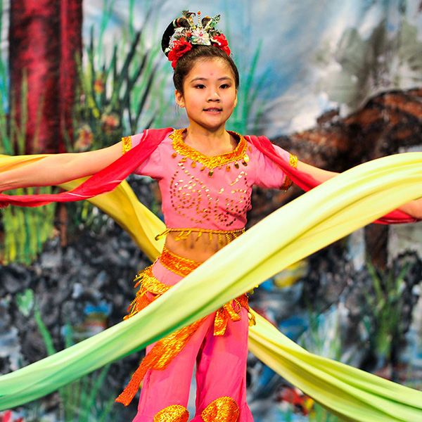 Young girl in an ornate pink and gold outfit, twirling colorful streamers.