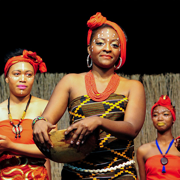 Women in orange and patterned clothing, holding wooden bowls.