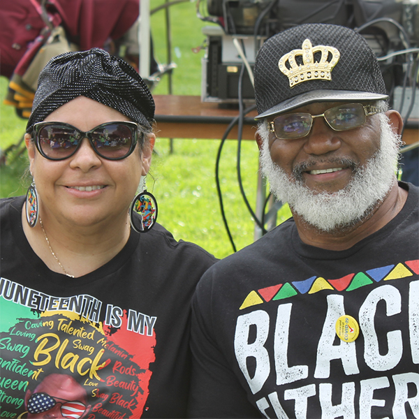 A black man and black woman smiling, sitting outside on a yard.