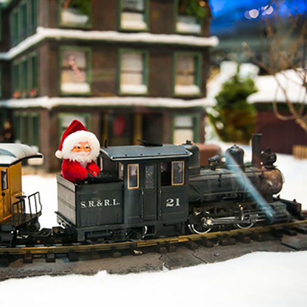 a Santa Claus rides atop a model train engine through a miniature village display