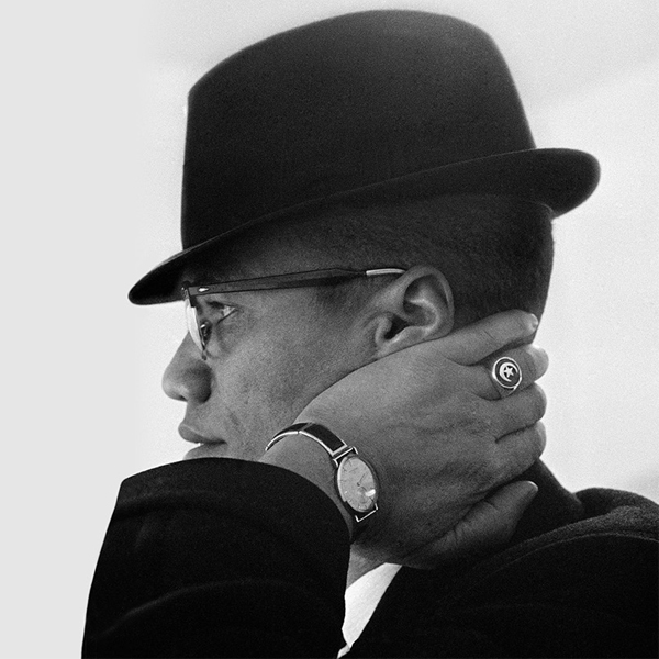 Photo of a man as Malcolm X holding his neck and looking to the left