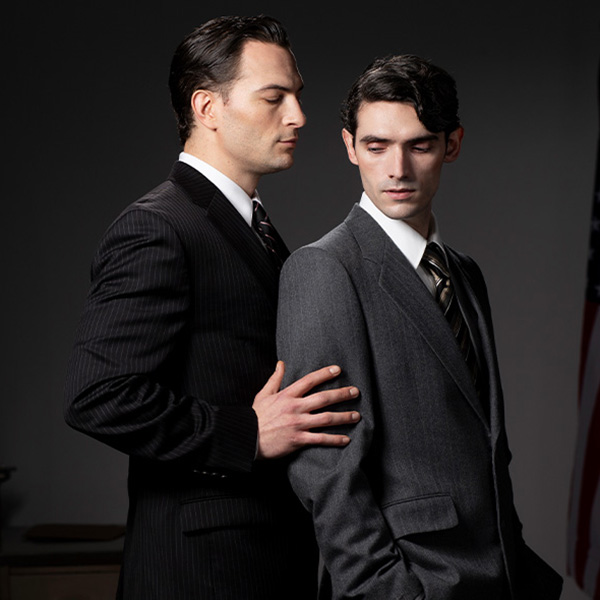 Two men dressed in formal suits, standing next to each other with a mysterious demeanor.