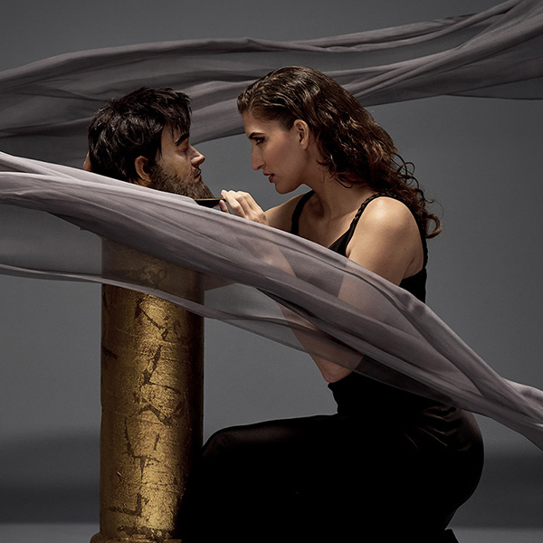 Woman in a black dress crouched and facing a man in a gold tube.